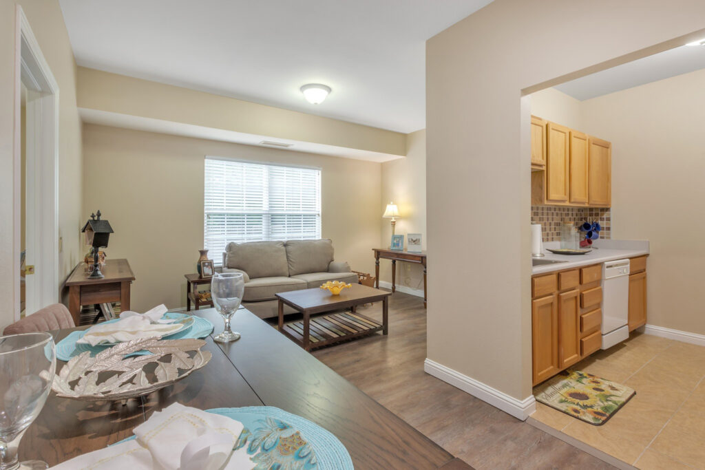 Hallway leading to a living room with a couch and a few side tables, and a kitchen with light brown cupboards at Town Village Tulsa, a senior living community near Broken Arrow offering independent living.