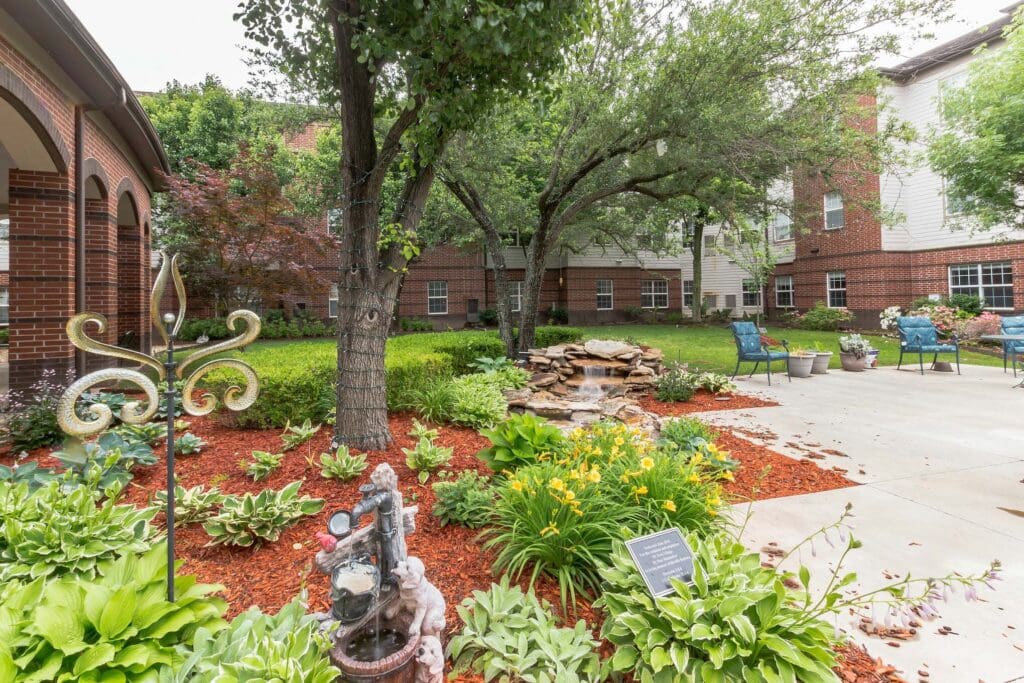 Town Village Tulsa outdoor courtyard with trees, a garden, a small fountain, and blue benches.