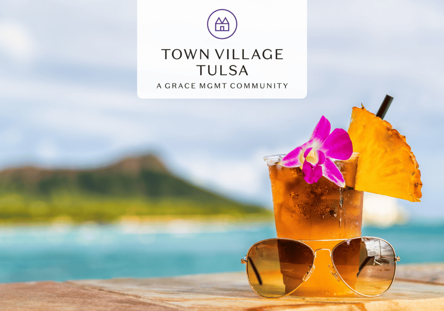Tropical cocktail with pineapple slice and pink orchid beside sunglasses on a wooden table by turquoise water; branding reads Town Village Tulsa.