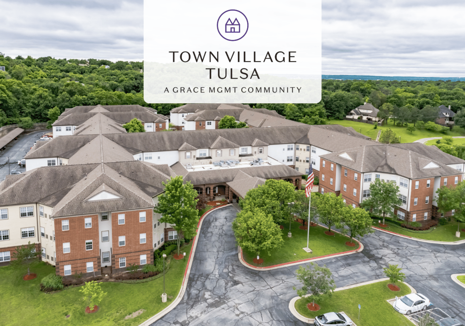 Aerial view of Town Village Tulsa residential campus with a translucent banner bearing the logo and text 'Town Village Tulsa' and 'A Grace MGMT Community' over the buildings.